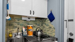 A compact kitchen with white cabinets, a tiled backsplash, and a blue towel hanging on the wall.