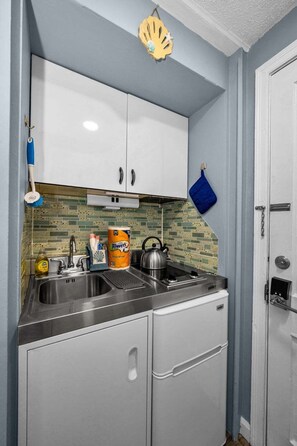 Una cocina compacta con armarios blancos, salpicadero de azulejos y una toalla azul colgada en la pared.