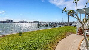 A waterfront view with a grassy area, a dock, and a marina in the background.