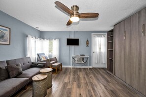 A living room with a sofa, two round side tables, a ceiling fan, a TV, and a door with a curtain.