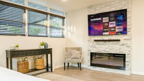 A modern living room with a fireplace, a flat-screen TV mounted on a stone wall, a comfortable armchair, and a console table with baskets. - Modern Relaxing Retreat w/ Pool, Fire pit, Game room (Orlando)