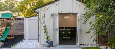 A small, white building with a 'GAME ROOM' sign, a green slide, and a pool table visible through the open door.