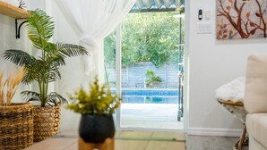 A room with a view of a swimming pool, a wicker plant, and a white chair. - Modern Relaxing Retreat w/ Pool, Fire pit, Game room (Orlando)
