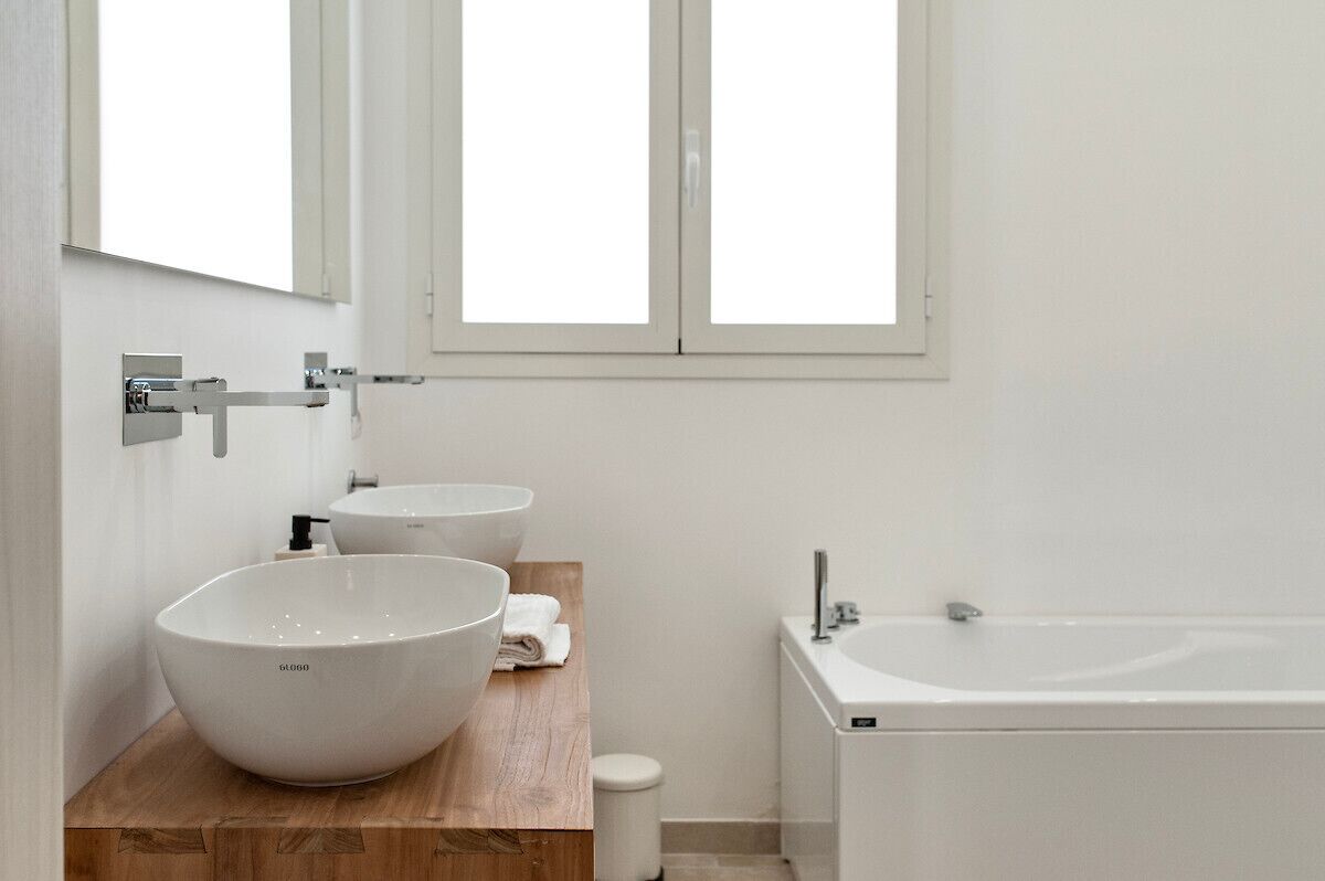 Un bagno moderno con una grande vasca da bagno bianca, due lavandini in ceramica bianca e un mobile contenitore in legno.