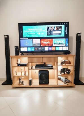 A television on a wooden stand with shelves below displaying various items.
