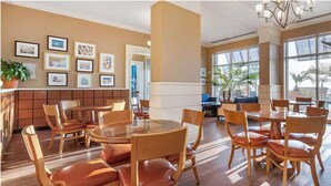 A spacious dining area with round tables and wooden chairs, framed artwork on the walls, and large windows allowing natural light. - Charming 1-bedroom bed & breakfast resort in awesome Virginia Beach (Virginia Beach)