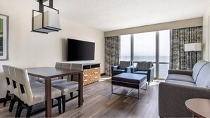 A modern hotel room with a dining area, a sofa set, a flat-screen TV, and a large window offering a view of the sea. - Charming 1-bedroom bed & breakfast resort in awesome Virginia Beach (Virginia Beach)