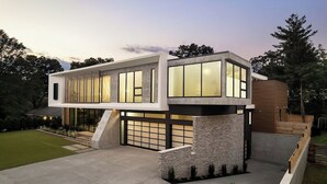 Een modern huis met twee verdiepingen, een plat dak, grote ramen en een stenen fundering.
