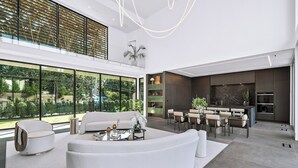Een moderne woonkamer met een gebogen witte bank, een eethoek met een glazen tafel en een keuken met donkere kastjes.