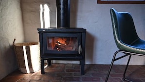 A wood-burning stove in a corner with a chair and a basket nearby. - Sue's House (Saint Andrews)