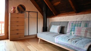 A cozy loft bedroom with a wooden floor, a grey sofa with a colorful blanket, a wooden dresser, and a black heater. - Sue's House (Saint Andrews)