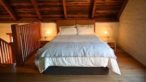 A cozy bedroom with a wooden ceiling, a large bed with a grey blanket, two bedside lamps, and a wooden railing. - Sue's House (Saint Andrews)