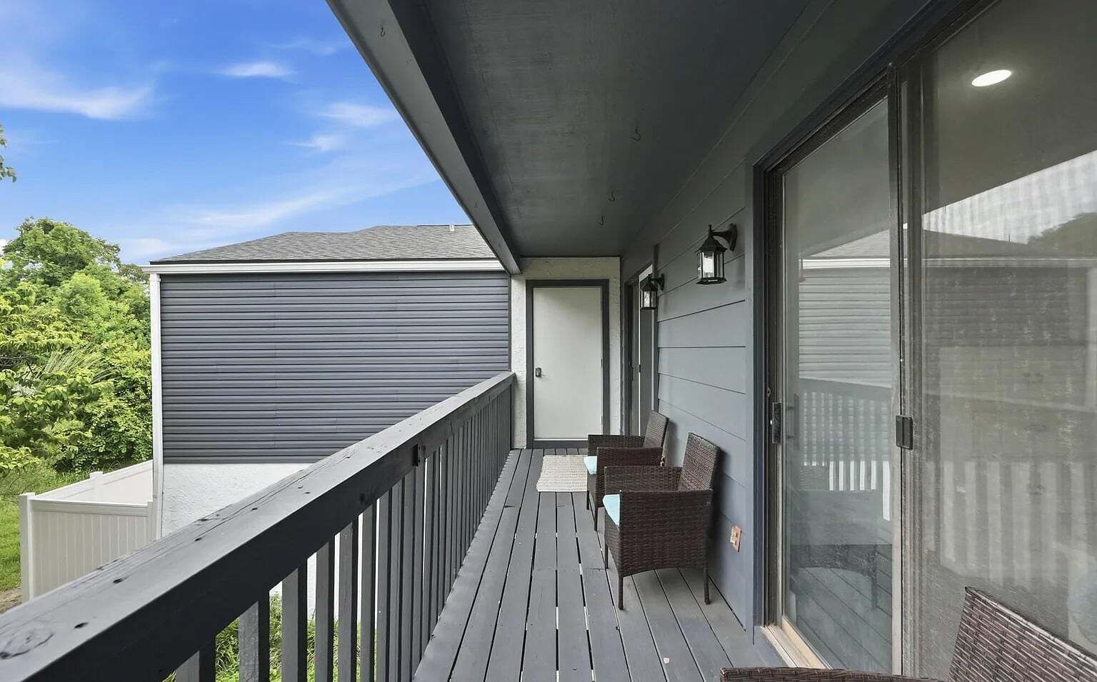 A balcony with a wooden railing, a seating area with wicker chairs, and a sliding glass door.