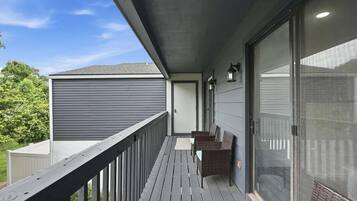 A balcony with a wooden railing, a seating area with wicker chairs, and a sliding glass door.