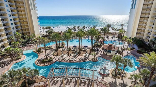 A resort with a pool area surrounded by palm trees and a view of the ocean.