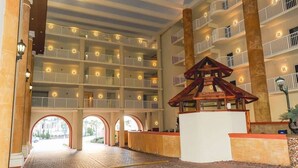 A multi-level hotel atrium with balconies, a central wooden structure, and a brick pathway leading to an archway.