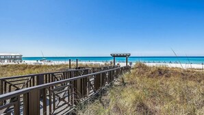 A wooden boardwalk leading to a beach with a gazebo and a small building in the background.