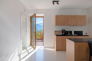 A modern kitchen with wooden cabinets, a black countertop, and a view of mountains through an open door.