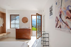 A bedroom with a wooden dresser, a bed, a window, and a door leading to a balcony.