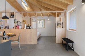 A modern interior with a wooden ceiling, a dining area with a table and chairs, a bench, and a bed in the background.