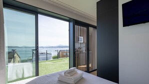 Ein modernes Zimmer mit einer großen Schiebeglas-Tür, die auf einen Balkon mit Blick auf das Meer und ferne Berge führt.