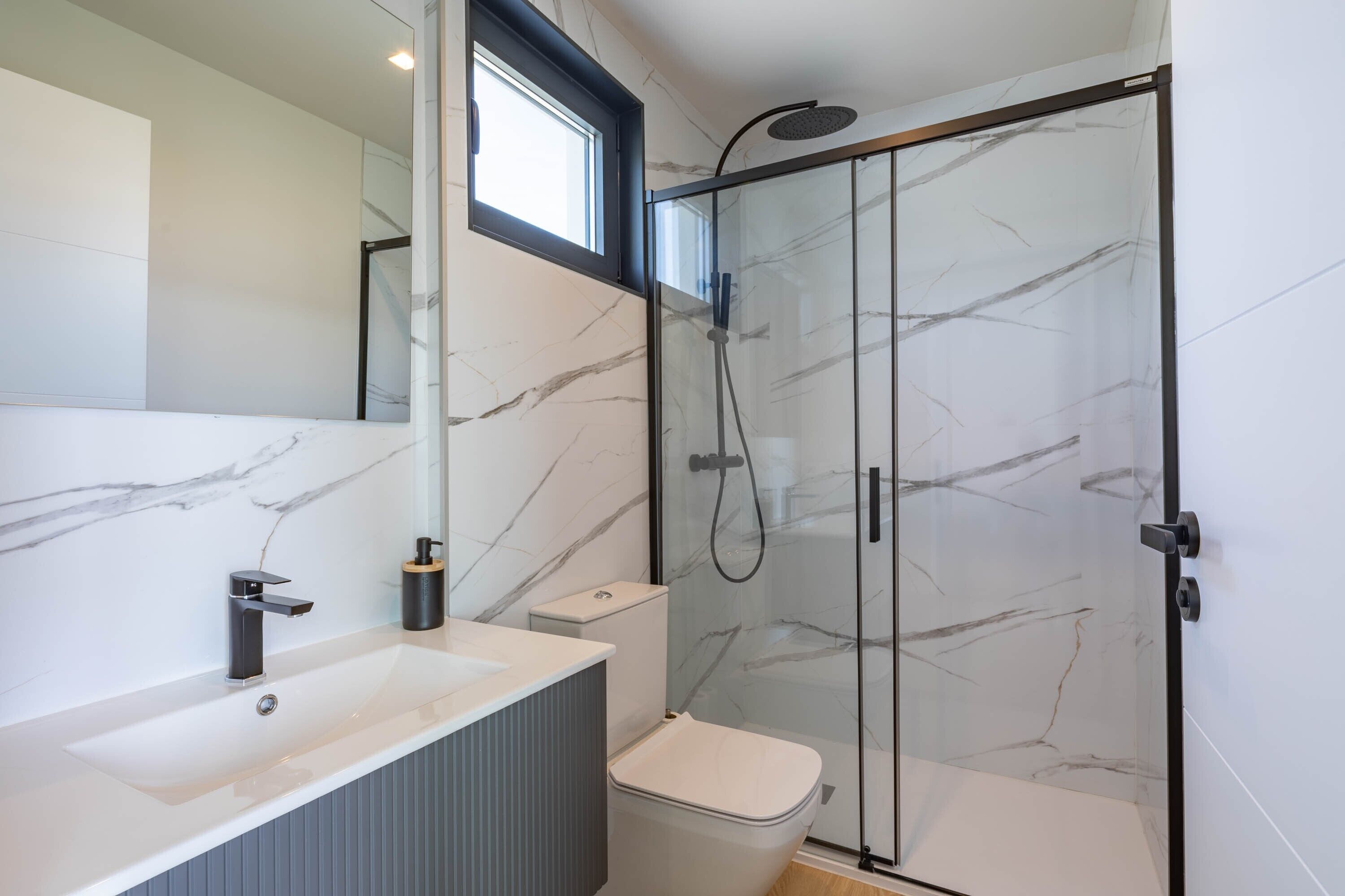 A modern bathroom with a glass-enclosed shower, a white sink, and a toilet.