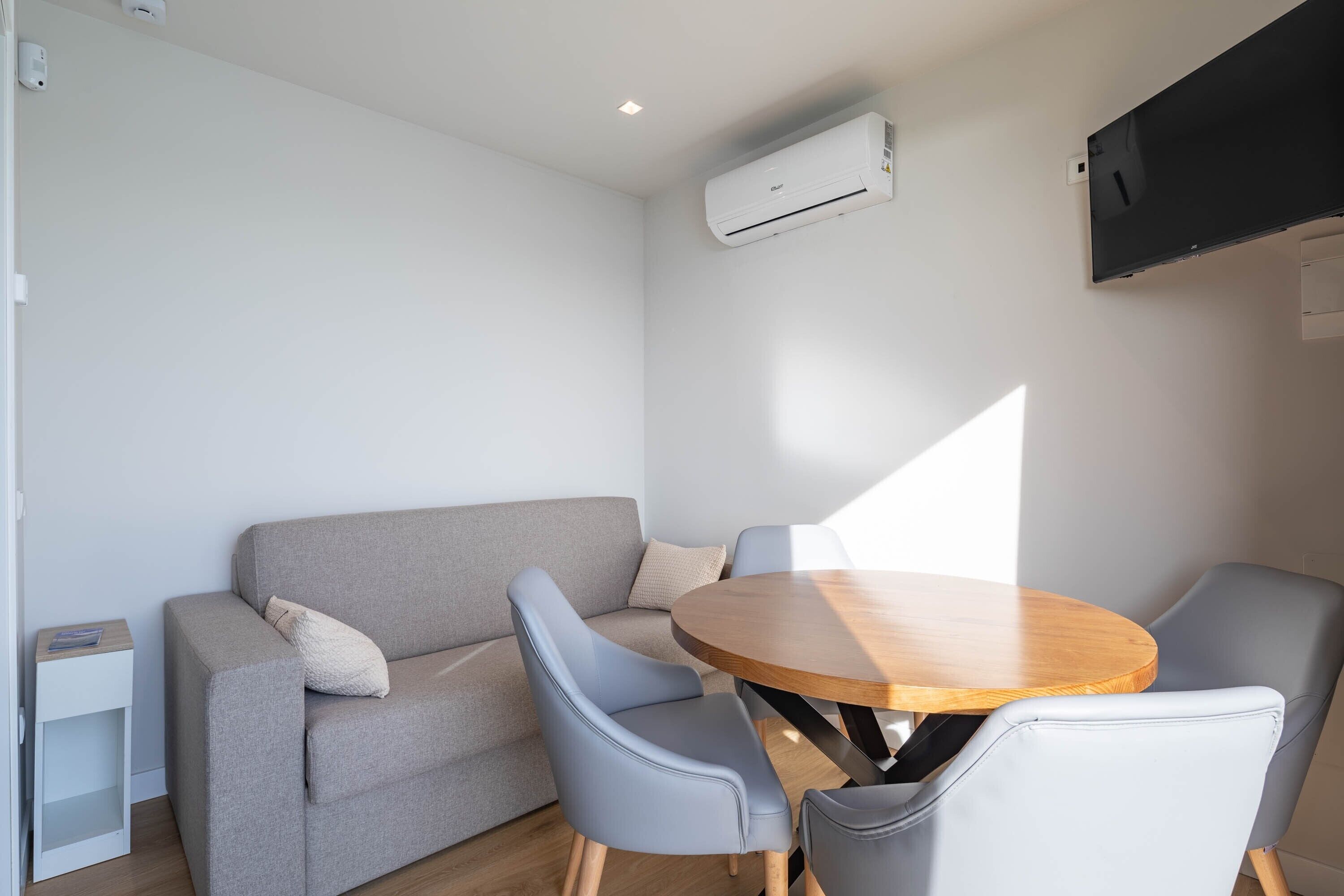 A modern room with a grey sofa, two grey chairs, a wooden table, and an air conditioning unit on the wall.