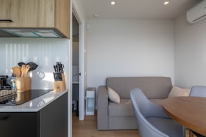Una cocina moderna con estufa integrada, un área de comedor con mesa redonda y un sofá gris.