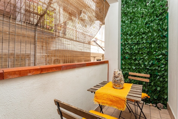A small outdoor seating area with a table and chairs, a decorative glass jar, and a green leafy wall.