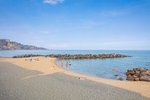 A beach with clear water, rocky shoreline, and people sunbathing.