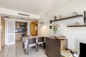 Une cuisine moderne avec un coin repas, des meubles en bois, une cuisinière encastrée et une étagère murale agrémentée d’objets décoratifs.