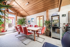 Una habitación con paneles de madera, una mesa y sillas, un refrigerador y plantas en macetas.
