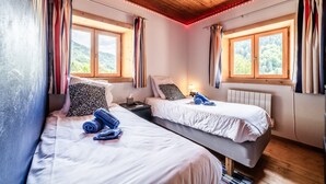 Ein Zimmer mit zwei Betten, einem Nachttisch, einer Lampe und einem Fenster mit Vorhängen.