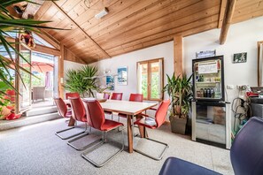 Une pièce aux murs lambrés, avec une table et des chaises, un réfrigérateur et des plantes en pot.