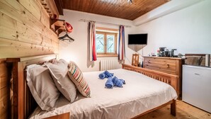 A wooden-paneled bedroom with a bed, a dresser, a television, and a window with curtains.