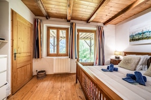 Quarto com painéis de madeira, uma cama, uma janela, um radiador e um cesto.
