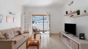 Ett modernt vardagsrum med en soffa, ett soffbord, en tv och hyllor med växter.