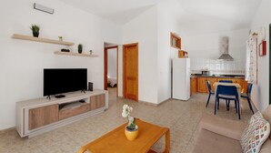 Ett vardagsrum med en TV, ett soffbord med en växt, en soffa och en matplats med stolar.