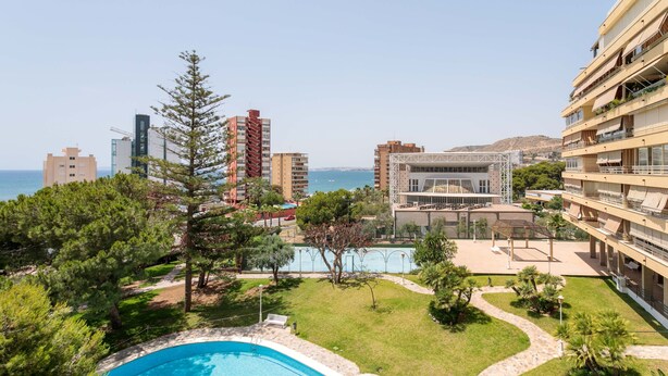 A pool surrounded by greenery, a building with balconies, and a view of the sea. - Apartment 'Vistas Al Mar' with Shared Pool, Wi-Fi and Air Conditioning (Alicante (Alacant))