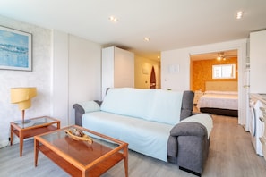 A modern room with a sofa, a glass coffee table, a lamp, a bed, and a washing machine.