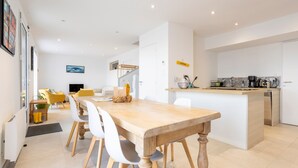 A modern kitchen with a central island, white cabinetry, and a dining area with a wooden table and chairs.