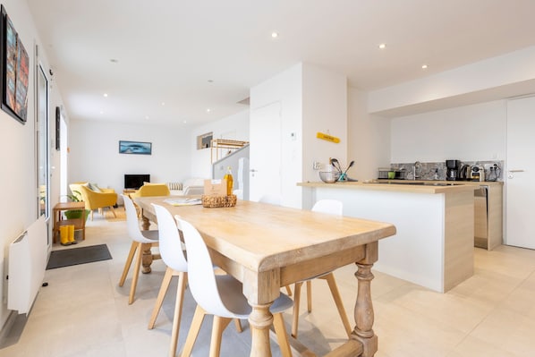 A modern kitchen with a central island, white cabinetry, and a dining area with a wooden table and chairs.
