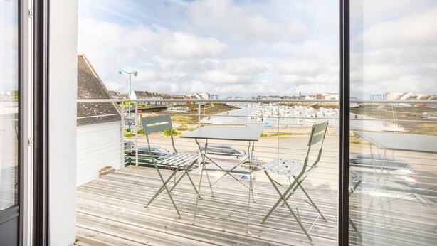 A balcony with a table and chairs, overlooking a marina with boats and buildings.