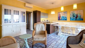 A room with a dining area, a kitchen, and a seating area with wicker furniture.