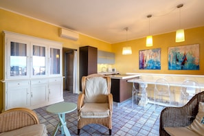 A room with a dining area, a kitchen, and a seating area with wicker furniture.