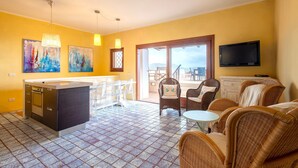 A modern kitchen with a central island, dining area with wicker furniture, and a TV mounted on the wall.