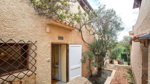 A narrow courtyard with a stone wall, a metal gate, and a door leading to a room.