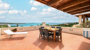 A terrace with a table and chairs, a sun lounger, and a view of the ocean.