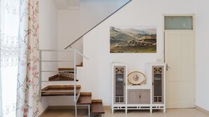 A staircase with a metal handrail, a white door, a cabinet with a decorative plate, and a landscape painting on the wall.