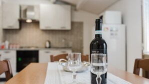 A bottle of wine and two glasses on a table in a kitchen with white cabinets and a tiled backsplash.
